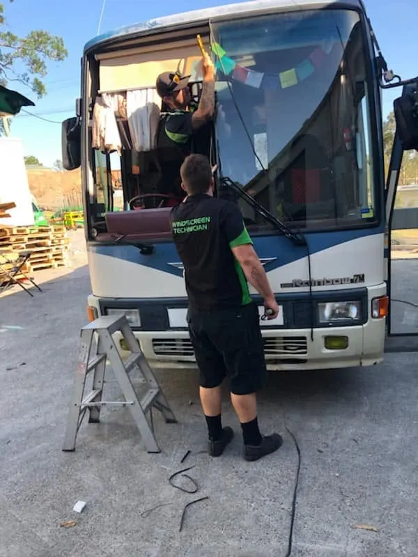 Two Express Auto Glass fitters replacing a coach windscreen from a step ladder