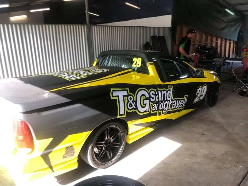 Sponsor-liveried race ute in a shed during windscreen work