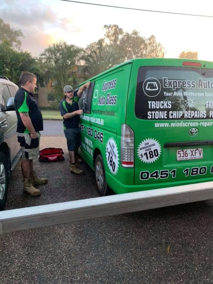 Two Express Auto Glass fitters working on the rear glass of a branded service van at dusk